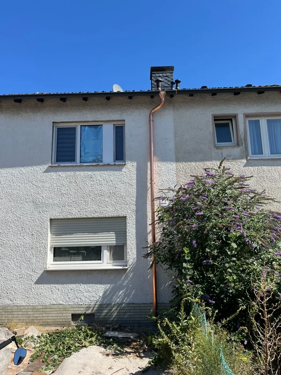 Neu montiertes kupferfarbenes Fallrohr an einer Hausfassade mit Anschluss an die Dachrinne